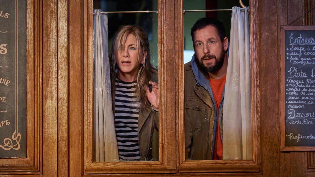 Audrey and Nick peer through a broken window in Murder Mystery 2, one of the new Netflix movies