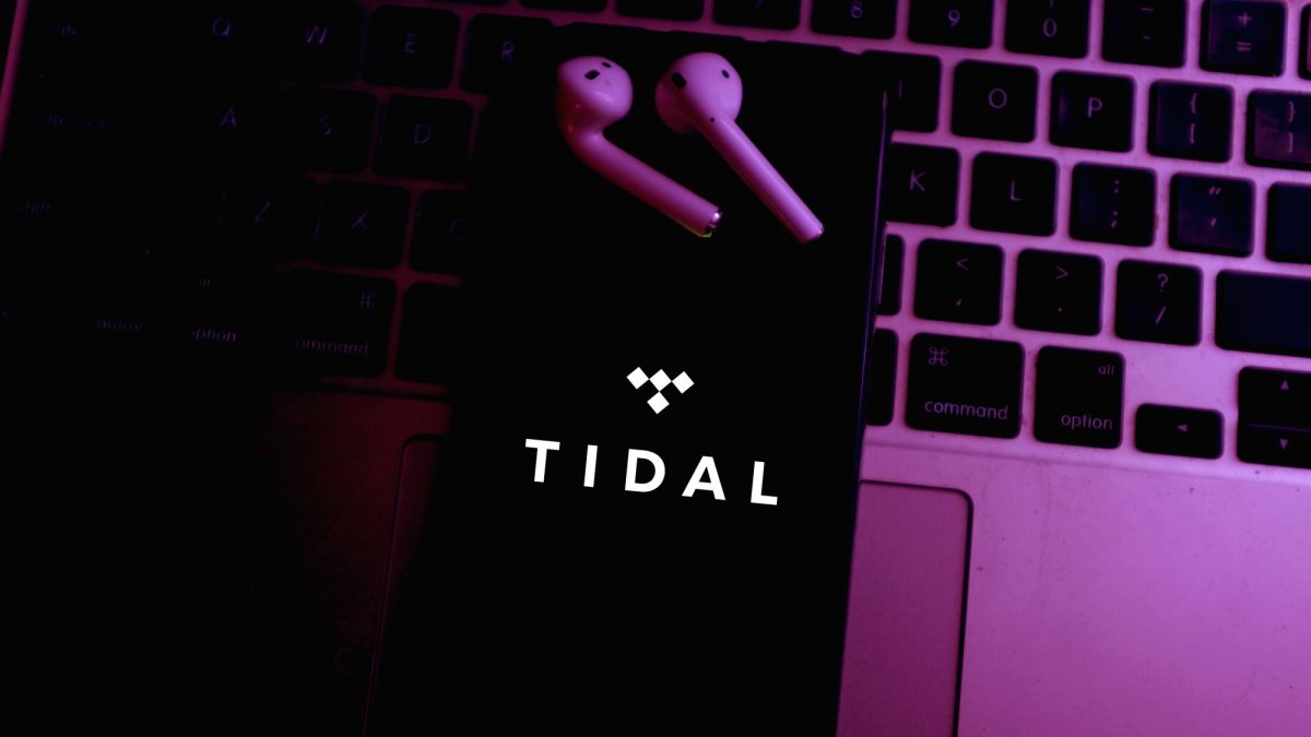 Smartphone with Tidal logo laying on a laptop keyboard with wireless earbuds next to it