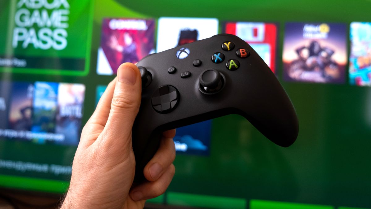 An Xbox Series X controller held in front of a TV showing the console
